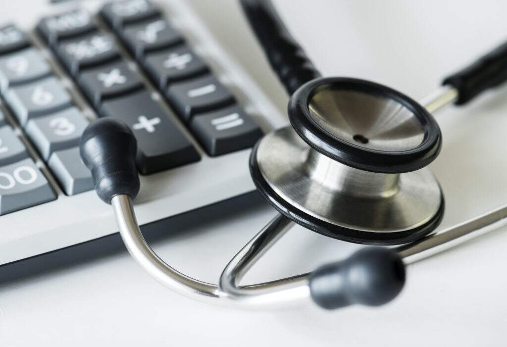 Closeup Of A Calculator And A Stethoscope Healthcare And Expense - Souza & Souza Contabilidade